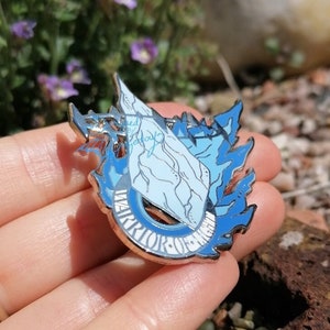 Peut inclure: Une épingle en émail bleu et argent avec une image stylisée d'une baleine avec une vague derrière elle. L'épingle dit "WARRIOR OF THE DEEP" autour de la baleine.