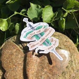 May include: A sticker featuring a green leaf and a sword, with the quote "Not all those who wander are lost".