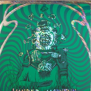 May include: A green and silver holographic concert poster for Yonder Mountain String Band. The poster features an illustration of a diver in a diving suit with fish swimming around them. The text "Yonder Mountain String Band" is written in a stylized font. The poster lists tour dates for the band in March and April 2023.