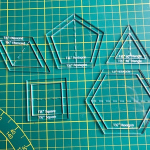 Op de afbeelding: Een set van transparante plastic patchwork sjablonen voor het maken van verschillende vormen, waaronder een ruit, een vijfhoek, een driehoek, een vierkant en een zeshoek. De sjablonen zijn gelabeld met hun vorm en maat in inches.