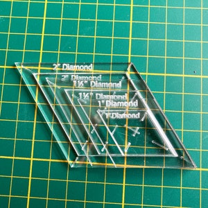 Op de afbeelding: Vier transparante, diamantvormige naai-linialen van plastic, gestapeld op elkaar. De linialen zijn gelabeld met de maten: 1/2" Diamant, 1" Diamant, 1 1/2" Diamant en 2" Diamant.