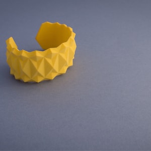 May include: A yellow geometric bangle bracelet with a textured surface.