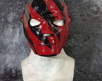 May include: A red and black wrestling mask with a textured leather finish. The mask has a menacing expression with a wide mouth and sharp teeth.