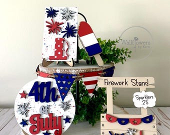 May include: Wooden 4th of July decorations with red, white, and blue colors. The decorations include a sign that says "Firework Stand", a sign that says "4th of July", a sign that says "America", and a sign that says "Sparklers .25".