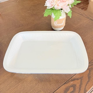 May include: A rectangular, off-white serving tray with a slightly raised, ribbed border. The tray has rounded corners and a thin, dark blue trim. A small vase with faux flowers and the word "blessed" is in the background.
