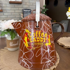 May include: A brown metal coffee pot with a white handle and lid. The pot has a white scribble design and the words "Coffee Caddy" in yellow and red. The text "Columbian Terre Haute, Indiana, U.S.A." is also visible.