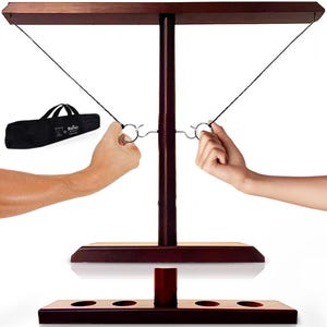May include: A dark wood ring toss game with a base, vertical support, and horizontal bar. Two hands are shown holding the rings. A black carrying bag is in the background.