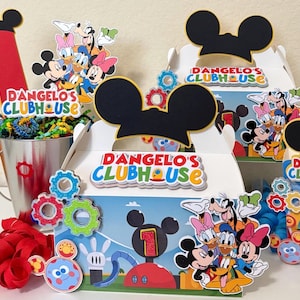 May include: Party decorations featuring Mickey Mouse and friends. Includes boxes with Mickey Mouse ears, the text "D'Angelo's Clubhouse", and character cutouts. A red number one and a metal bucket with colourful filler are also present.