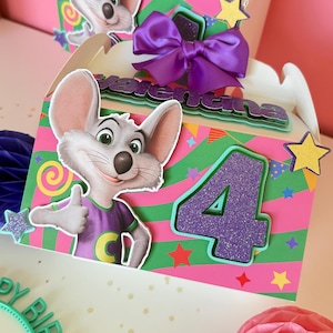 May include: A birthday gift box featuring a cartoon mouse character giving a thumbs up. The box is decorated with a large number 4, a purple bow, and the name "Valentina". The box has a pink and green striped background with star accents.
