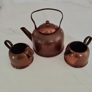 May include: A copper tea set with a teapot, creamer, and sugar bowl. The set is in a traditional style with a rounded shape and a polished finish.