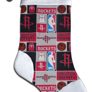 Peut inclure: Une chaussette de Noël blanche avec un revers rouge et un nom personnalisé "Brian". La chaussette est décorée d'un motif répété de logos des Houston Rockets, de ballons de basket et de maillots.