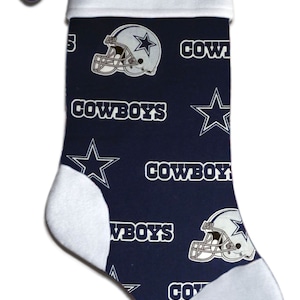 May include: A blue and white Christmas stocking with a Dallas Cowboys theme. The stocking has a white cuff with the name "Brian" embroidered on it. The stocking is decorated with a repeating pattern of the Cowboys star, the team's logo, and the word "Cowboys".