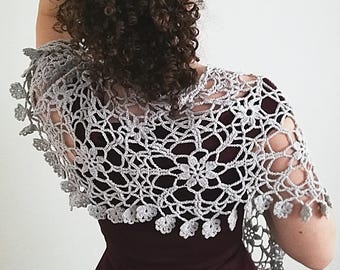 May include: A gray crocheted shawl with a delicate floral pattern. The shawl is draped over the shoulders of a person wearing a burgundy dress.