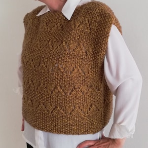 May include: A brown sleeveless knitted vest with a diamond pattern. The vest has a round neckline and is made of a soft, textured yarn.
