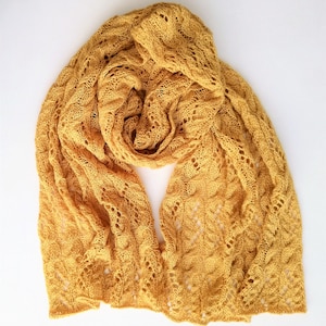May include: A yellow knitted scarf with a delicate openwork pattern. The scarf is made of a soft, lightweight yarn and has a flowing drape.