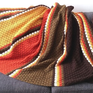 May include: A crocheted throw blanket with stripes of brown, orange, yellow, and white. The blanket is folded and draped over a couch.