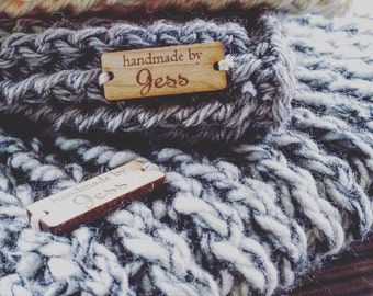 May include: Close-up of three handmade knitted items in cream, grey, and white. Each item has a wooden tag that reads "handmade by Jess". The knitted items appear to be soft and chunky, with a textured appearance.