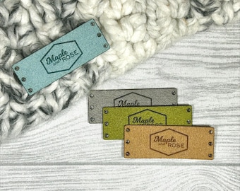 May include: A collection of rectangular labels in various colors, including blue, gray, green, and tan. Each label features the text "Maple and Rose" within a hexagonal design. The labels are riveted at each corner.