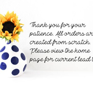 May include: A white vase with blue polka dots holds a bright yellow sunflower. The image includes the text: "Thank you for your patience. All orders are created from scratch. Please view the home page for current lead times."