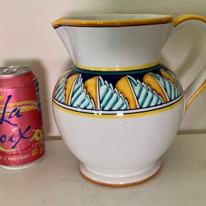 May include: White ceramic jug with a yellow, blue and green geometric design. The jug has a wide mouth and a handle.