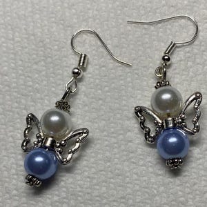 K&ouml;nnte beinhalten: Ein Paar silberne Engelsfl&uuml;gel-Ohrringe mit einer wei&szlig;en Perle und einer hellblauen Perle an jedem Ohrring.
