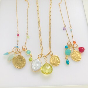 Puede incluir: Tres collares de oro con abalorios de piedras preciosas de colores. Cada collar presenta un estilo de cadena diferente y una variedad de abalorios, incluyendo monedas, cuentas y piedras. Los abalorios son en tonos de azul, verde, rojo y naranja.