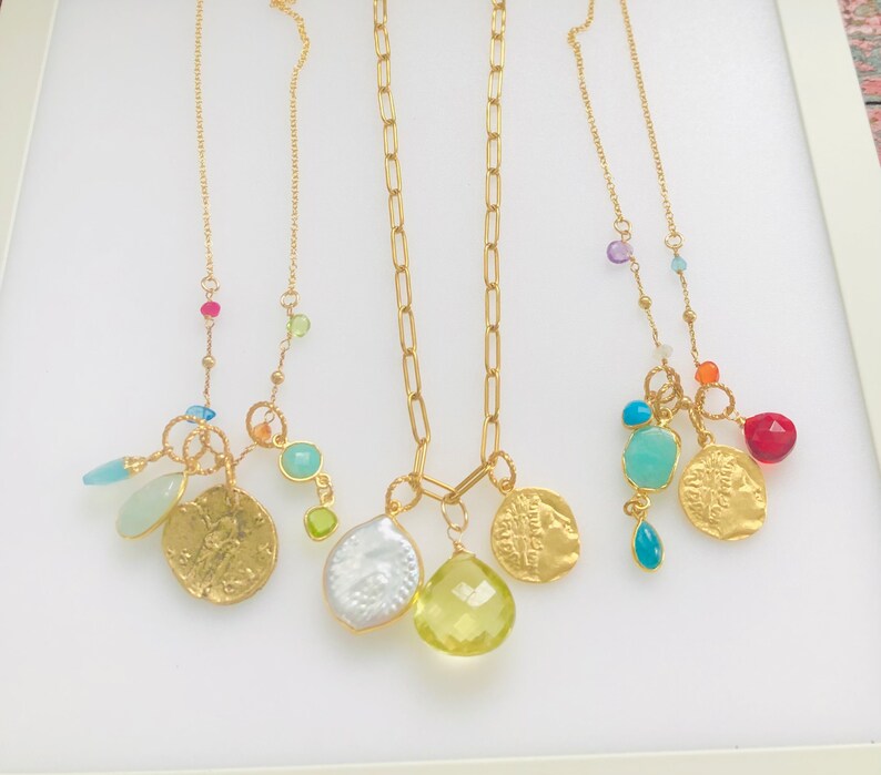 Puede incluir: Tres collares de oro con abalorios de piedras preciosas de colores. Cada collar presenta un estilo de cadena diferente y una variedad de abalorios, incluyendo monedas, cuentas y piedras. Los abalorios son en tonos de azul, verde, rojo y naranja.