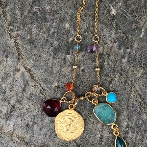 Puede incluir: Un collar de cadena de oro con una variedad de piedras preciosas de colores, incluyendo turquesa, amatista y cornalina. El collar presenta un gran colgante de moneda de oro con un dise&ntilde;o detallado.