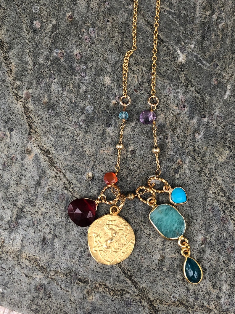 Puede incluir: Un collar de cadena de oro con una variedad de piedras preciosas de colores, incluyendo turquesa, amatista y cornalina. El collar presenta un gran colgante de moneda de oro con un dise&ntilde;o detallado.
