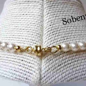May include: A close-up of a white pearl necklace with a gold clasp. The necklace is on a white fabric background. The text "Sobenvy" is visible in the upper right corner of the image.