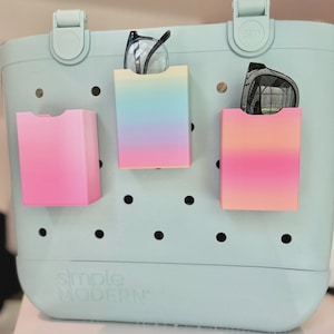 May include: A pale blue tote bag with three colourful, rectangular pockets attached. Each pocket has a gradient of colours, and two pairs of spectacles are stored in two of the pockets. The bag has the words "simple MODERN" printed on the front.