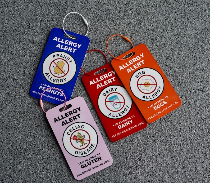 May include: Four colorful allergy alert tags with white text and graphics. The tags are blue, red, orange, and pink. Each tag has a different allergy warning: peanuts, dairy, eggs, and gluten. Each tag has a loop for attaching.