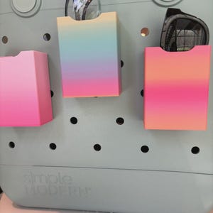 May include: A pale blue tote bag with three gradient-coloured storage pockets. One pocket is pink, and the other two are a mix of pink, orange, blue, and yellow. Eyeglasses and sunglasses are stored in the pockets. The bag has the words "Simple Modern" printed on it.