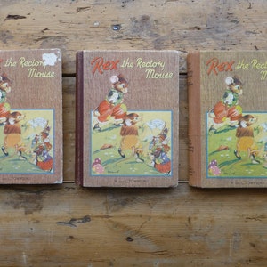 Könnte beinhalten: Drei identische gebundene Bücher mit dem Titel "Rex the Rectory Mouse" mit Illustrationen von Mäusen auf dem Cover. Die Bücher sind braun mit rotem Rücken und in einer Reihe auf einer Holzoberfläche angeordnet.