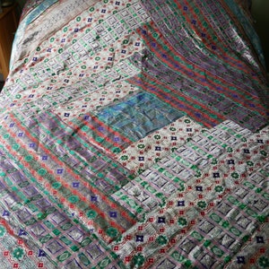 May include: A silver and white patchwork quilt with a geometric pattern in shades of green, blue, red, and purple.