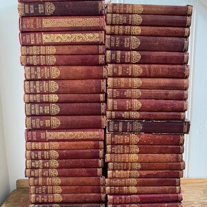 May include: A stack of over 40 vintage hardback books with burgundy covers and gold lettering. The books are arranged vertically with the spines facing outward. The books are all different sizes and have different titles.