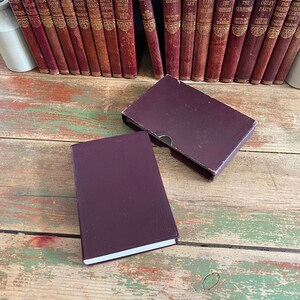 May include: A collection of vintage hardback books with burgundy covers and gold lettering. The books are arranged in two rows on a wooden surface. The titles of the books include "Rob Roy", "Waverley", "The Claverings", "Orley Farm", "The Innocents Abroad", and "The World Eight Days".
