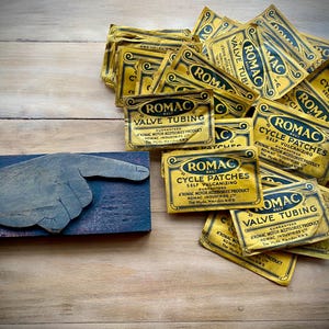 May include: A pile of yellow and black paper packets with the text "ROMAC" and "CYCLE PATCHES" and "VALVE TUBING".