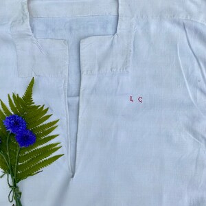 May include: White linen shirt with a V-neck and the initials "L.C." embroidered in red thread.