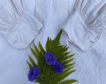 May include: White linen shirt with gathered cuffs and a fern with purple flowers.