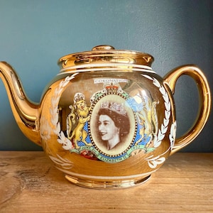 May include: Gold teapot with a commemorative design for Queen Elizabeth II's coronation. The teapot features a portrait of the Queen, the royal coat of arms, and the text "Coronation June 2nd 1953 Elizabeth II".