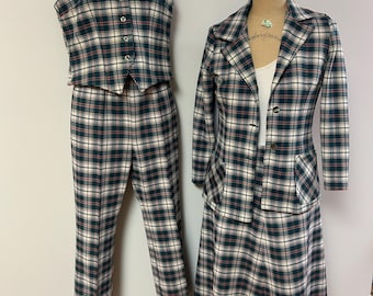 May include: A vintage plaid suit set featuring a vest, pants, and a blazer with a matching skirt. The set is in a green, red, and cream plaid pattern. The vest has buttons, and the blazer has a two-button closure.