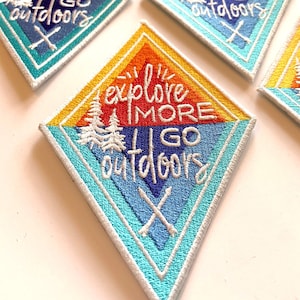 May include: Five diamond-shaped embroidered patches with the text "explore more I go outdoors" in a rainbow color scheme. The patches have a white background and are surrounded by a white border.