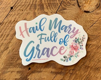 May include: A white sticker with a blue, pink, and purple gradient design that says "Hail Mary Full of Grace" with floral accents.
