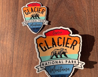 Peut inclure: Deux autocollants du parc national de Glacier avec un motif de chaîne de montagnes coloré et une silhouette d'ours. Le texte sur les autocollants indique "Explorer le parc national de Glacier Montana Est 1910".