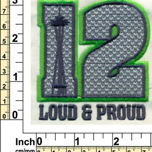 Puede incluir: Parche bordado verde y gris con el n&uacute;mero 12 y las palabras "Loud & Proud". El n&uacute;mero 12 est&aacute; en una fuente estilizada con un patr&oacute;n gris y blanco. El parche mide aproximadamente 5 cm de ancho.