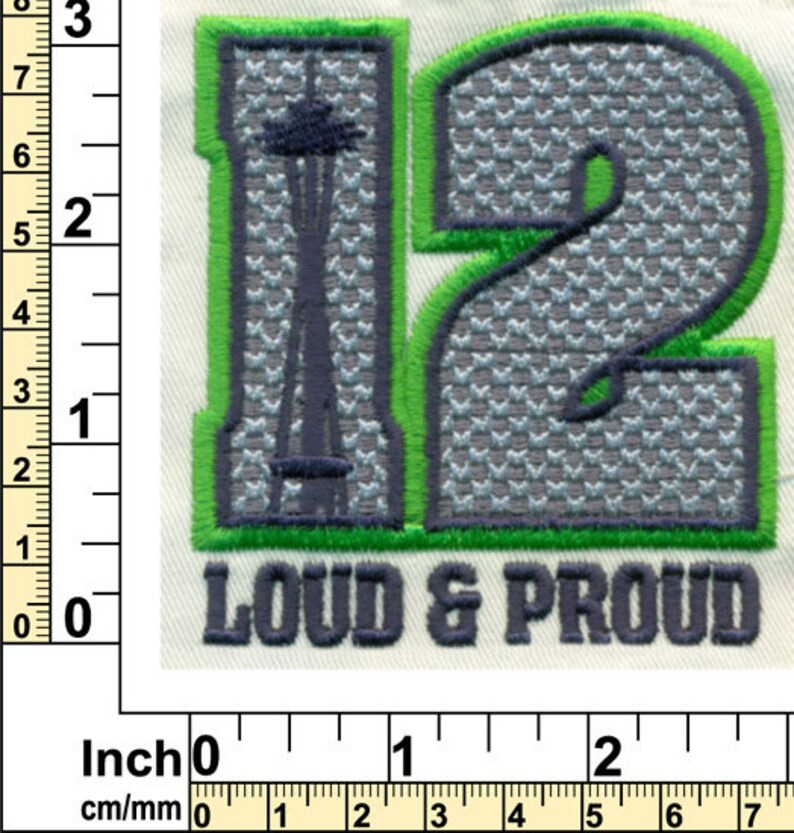 Puede incluir: Parche bordado verde y gris con el n&uacute;mero 12 y las palabras "Loud & Proud". El n&uacute;mero 12 est&aacute; en una fuente estilizada con un patr&oacute;n gris y blanco. El parche mide aproximadamente 5 cm de ancho.