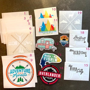 May include: Assortment of 19 stickers featuring various designs, including a camper van, a mountain range, a fish, a deer, and a dog. The stickers are printed on white paper and have a variety of colors and designs.
