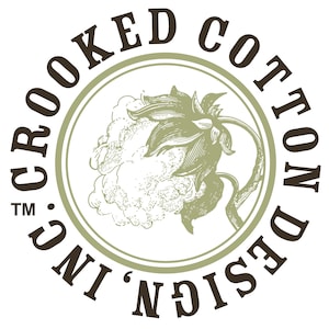 Op de afbeelding: Cirkelvormig logo met de tekst "CROOKED COTTON DESIGN, INC." in een bruin, schreeflettertype. Het logo toont een gedetailleerde illustratie van een katoenplant in groen- en wittinten, omsloten door een groene cirkel.