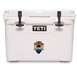 May include: A white YETI cooler with black latches and the Yellowstone National Park logo. The cooler is rectangular and designed for outdoor use. The YETI logo is displayed on the front.